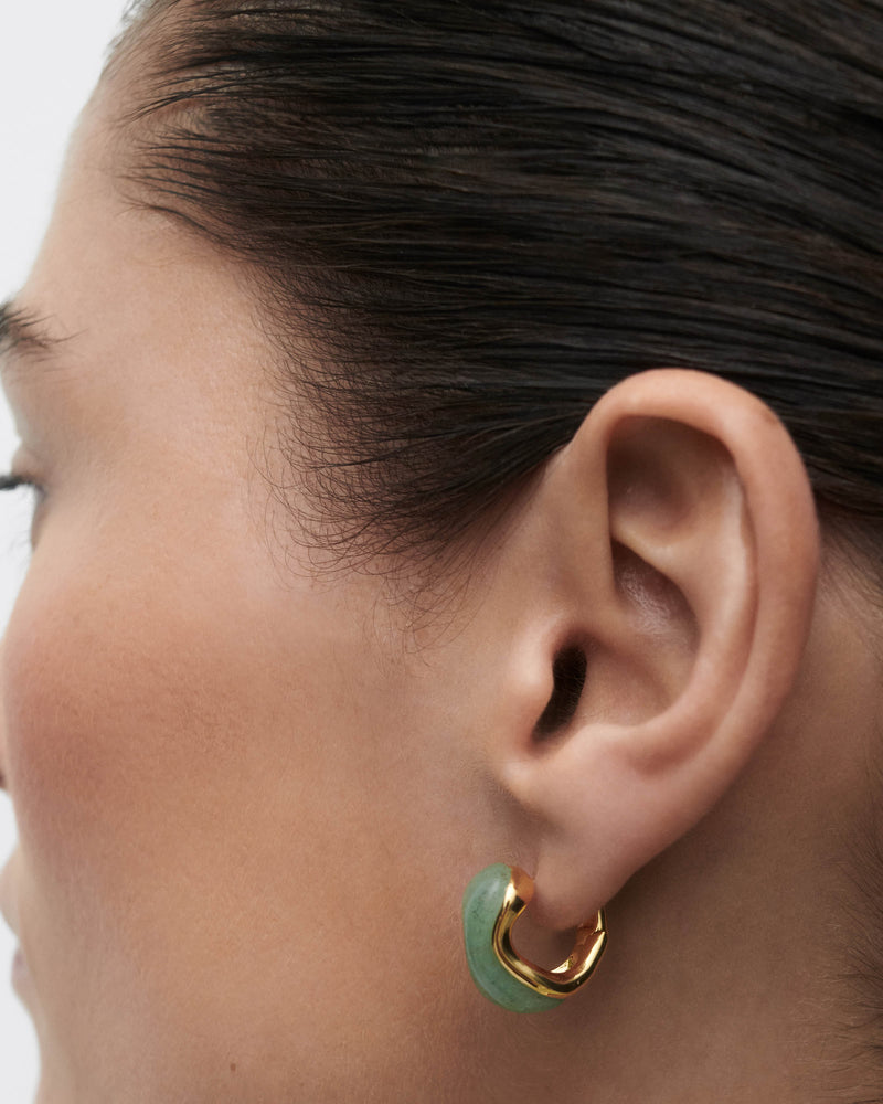 Gold-plated fluid huggie earrings with a curved green gemstone